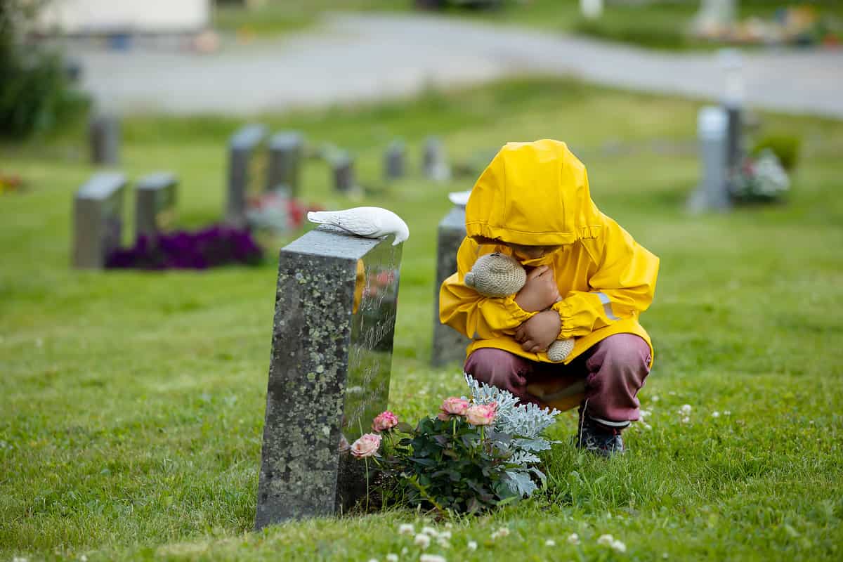 Een kind in een gele regenjas omringd door automatische concepten, geknield op een kerkhof.