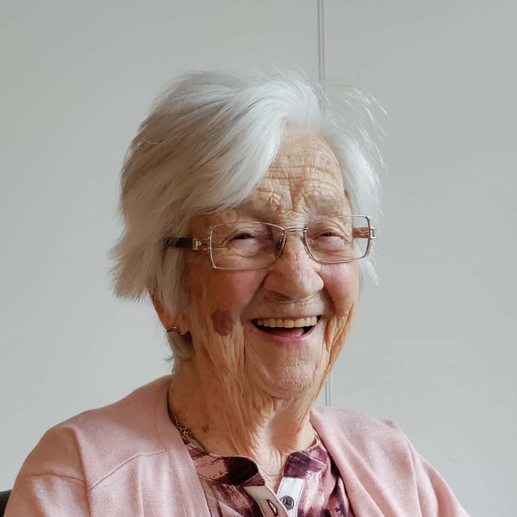 Een oudere vrouw met een bril en een roze trui, liefkozend Plonie genoemd.